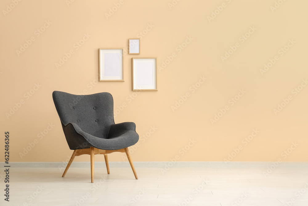 Stylish black armchair and frames near beige wall