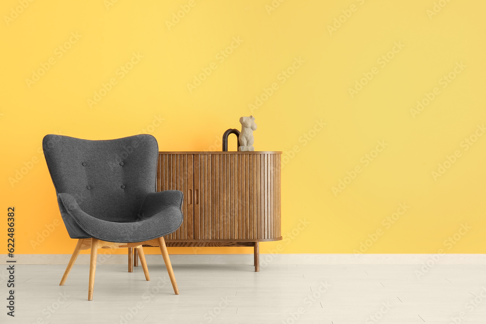 Stylish black armchair and cabinet with statue near yellow wall