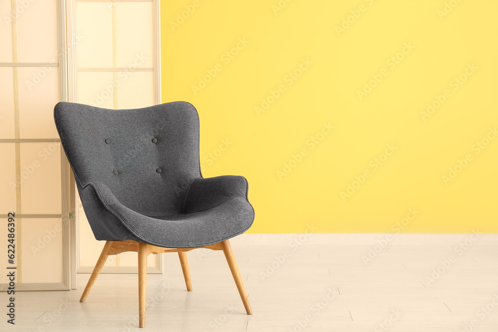 Stylish black armchair and folding screen near yellow wall