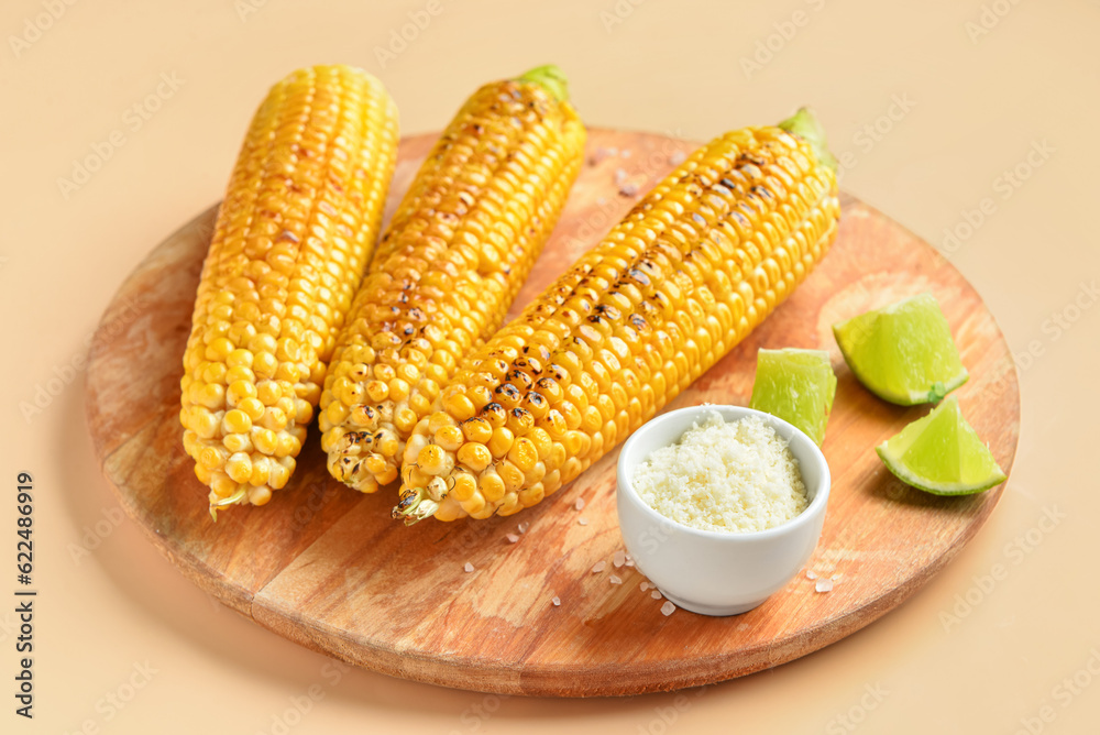 Wooden board with tasty grilled corn cobs and bowl of cheese on orange background