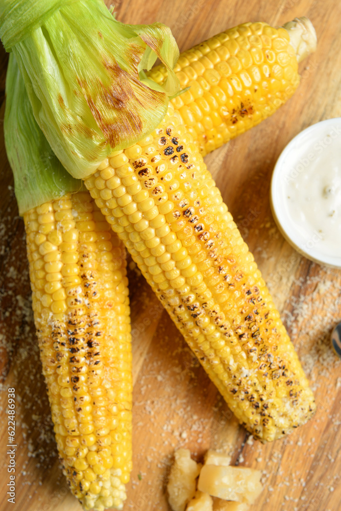 Tasty grilled corn cobs and sauce on wooden background