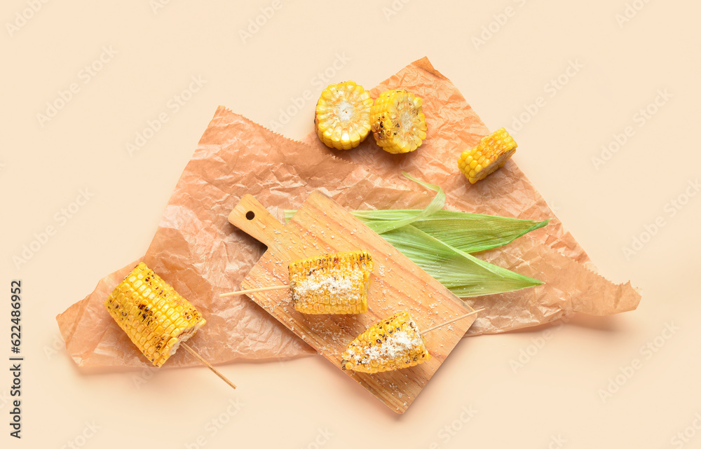 Wooden board with tasty grilled corn cob skewers on yellow background