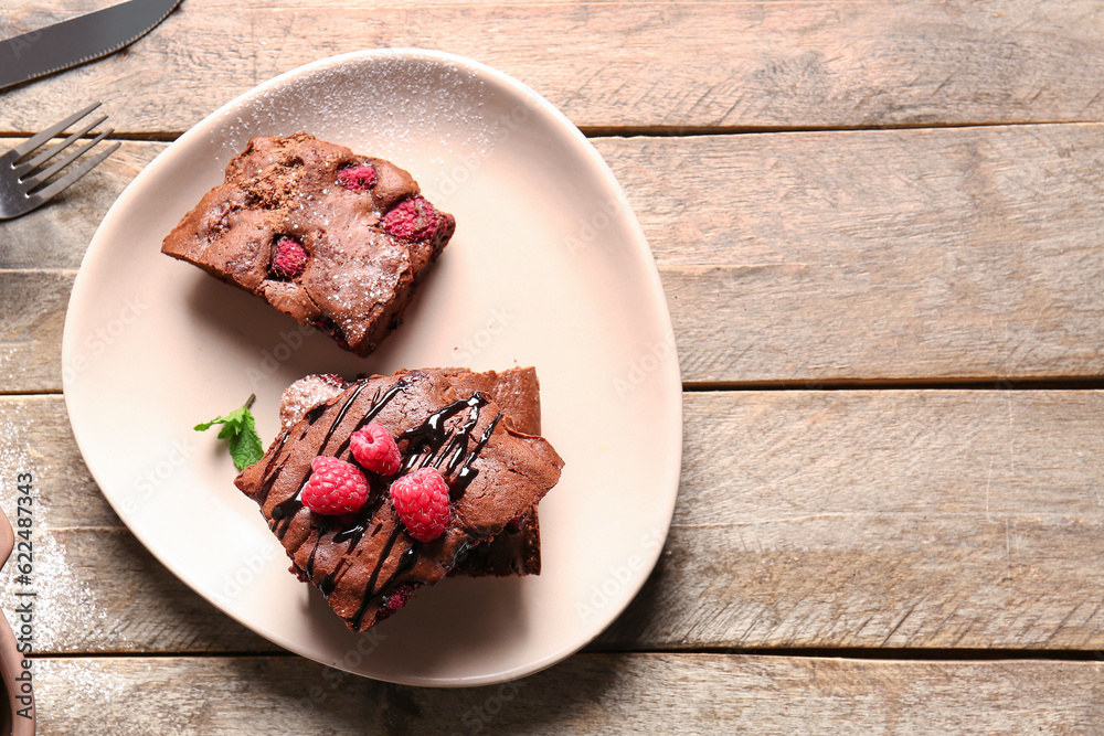 Plate with pieces of raspberry chocolate brownie on wooden table