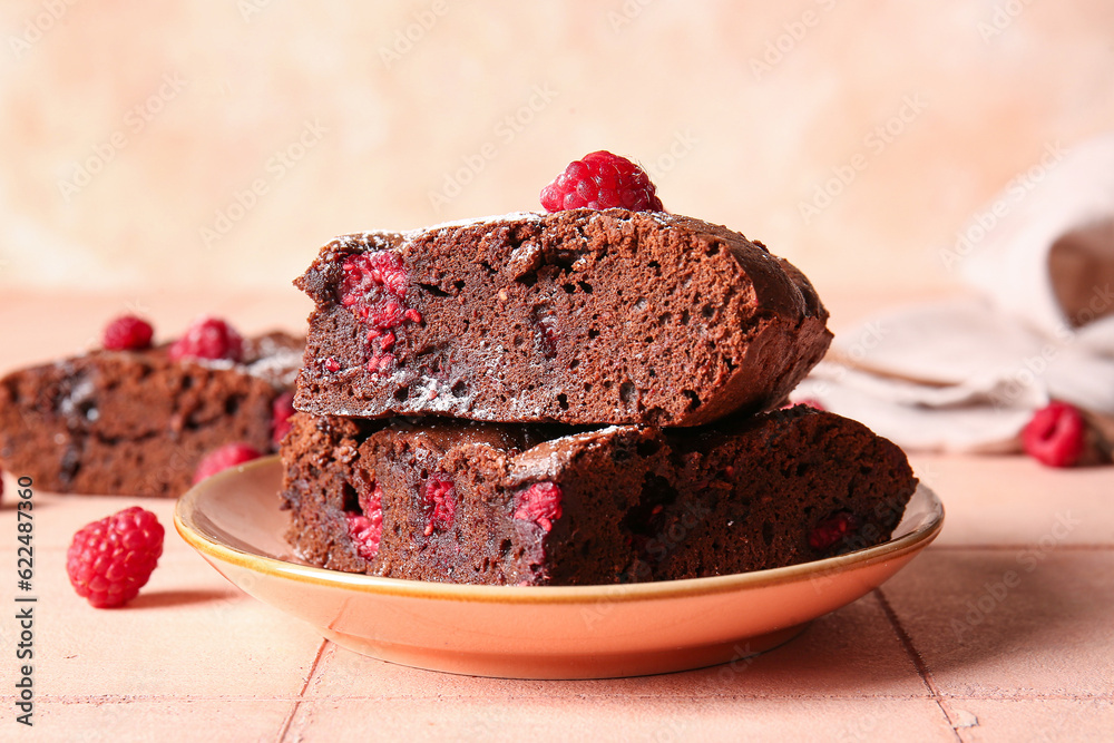 Plate with pieces of raspberry chocolate brownie on pink tile table