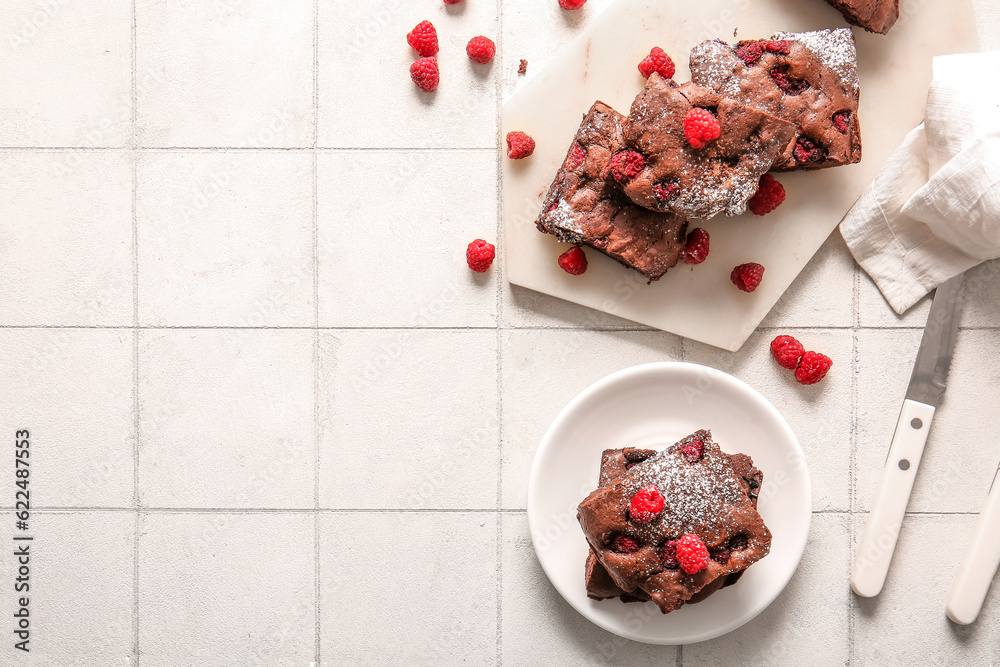 Board and plate with pieces of raspberry chocolate brownie on white tile background