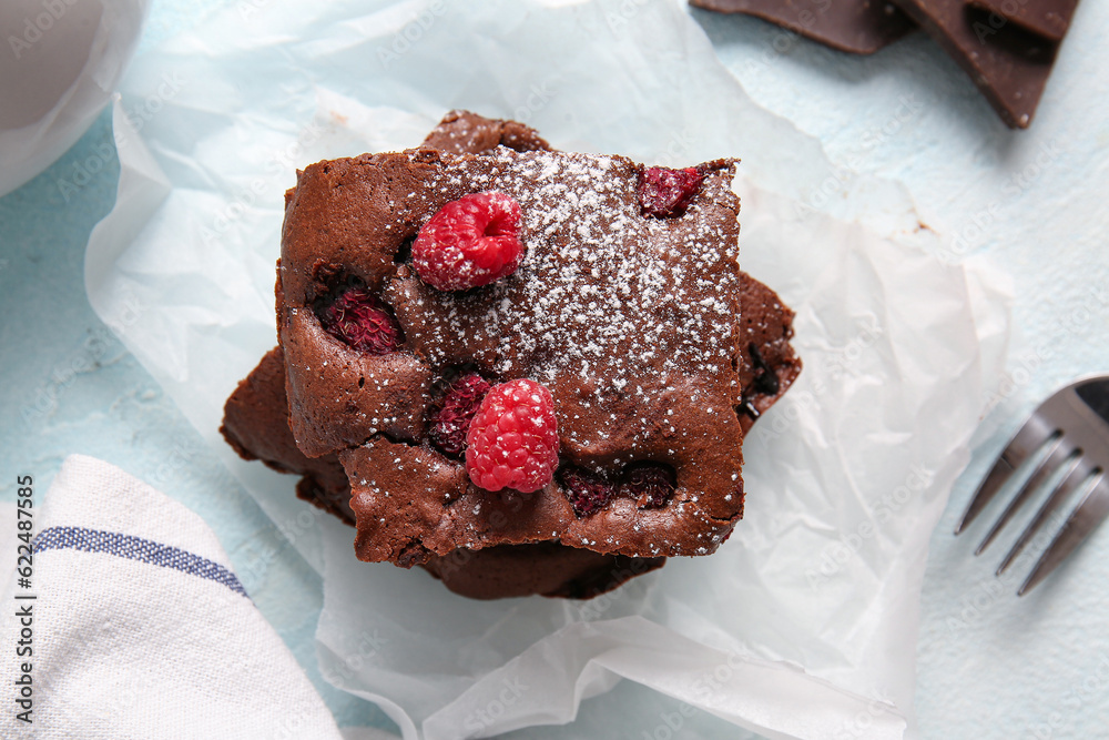 Baking paper with pieces of raspberry chocolate brownie on light blue table