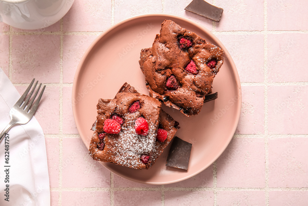 Plate with pieces of raspberry chocolate brownie on pink tile table