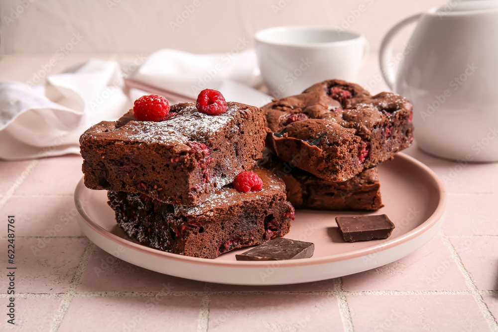 Plate with pieces of raspberry chocolate brownie on pink tile table