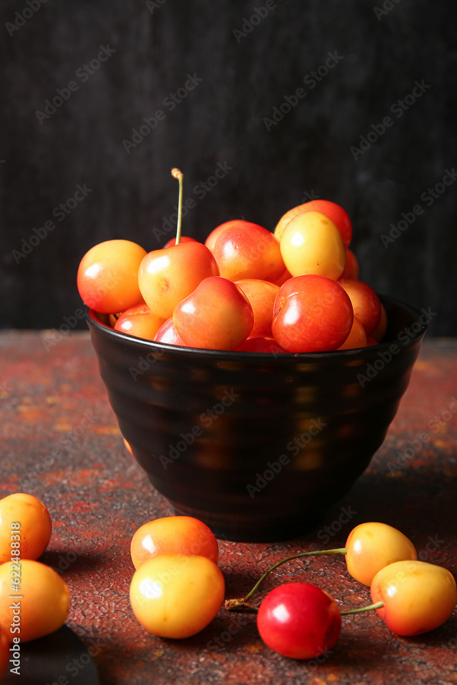 Bowl with sweet yellow cherries on dark table