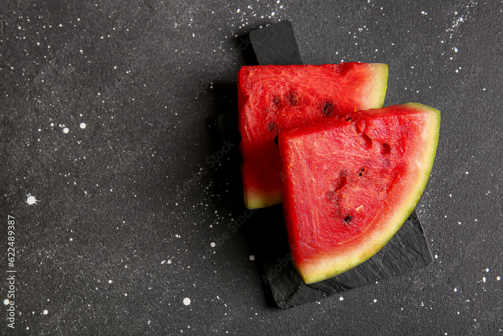 Board with pieces of fresh watermelon on black background