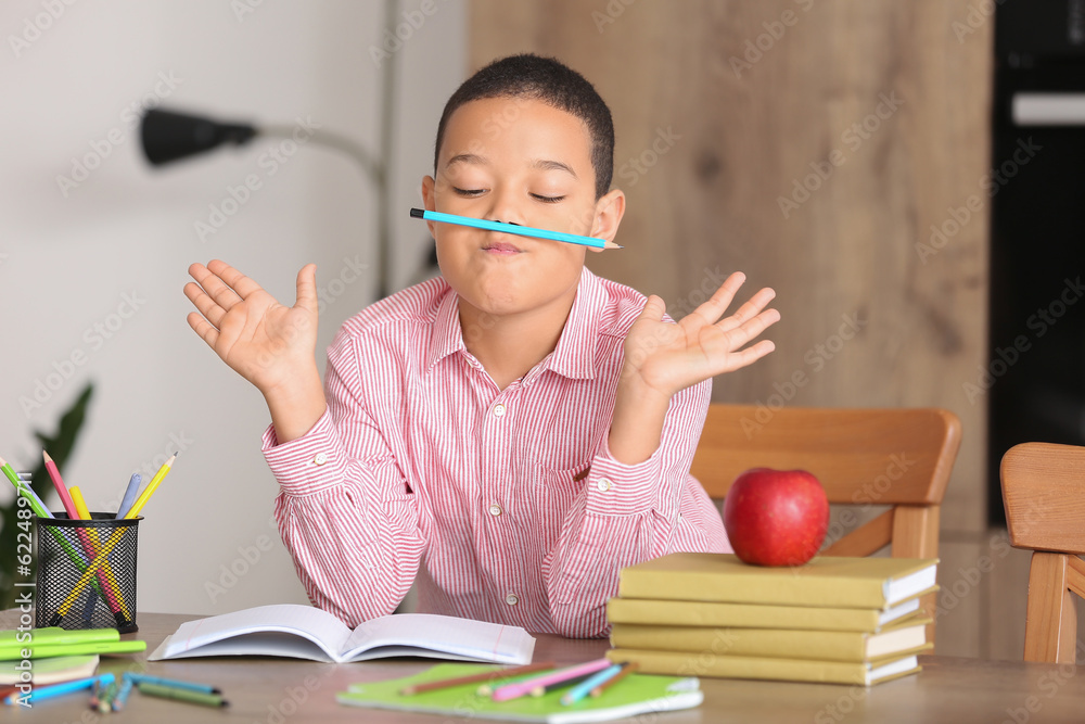 Funny little African-American boy doing homework in kitchen