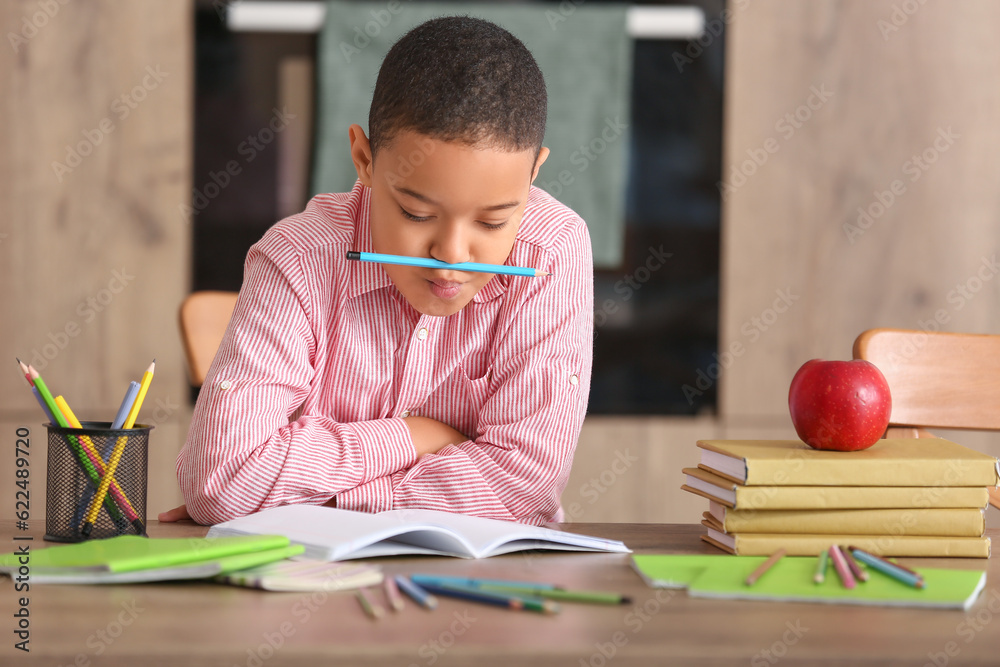 Funny little African-American boy doing homework in kitchen