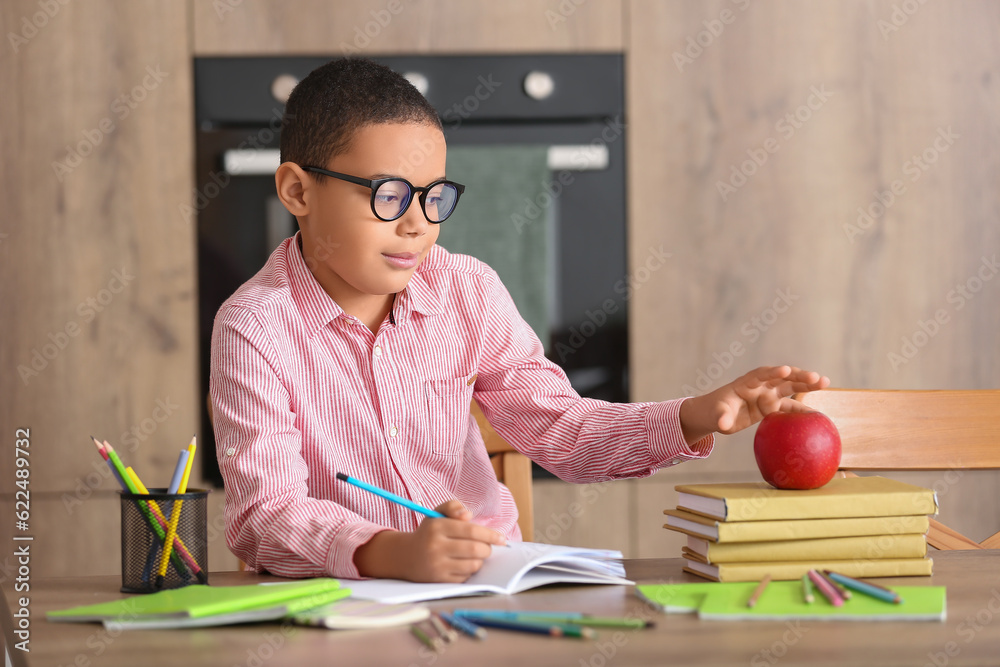 Little African-American boy with apple doing homework in kitchen