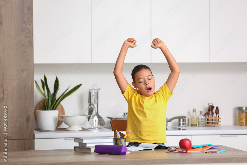 Tired little African-American boy doing homework in kitchen