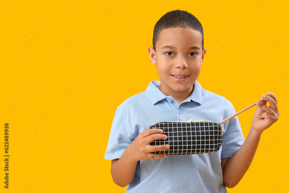 Little African-American boy with pencil case on orange background