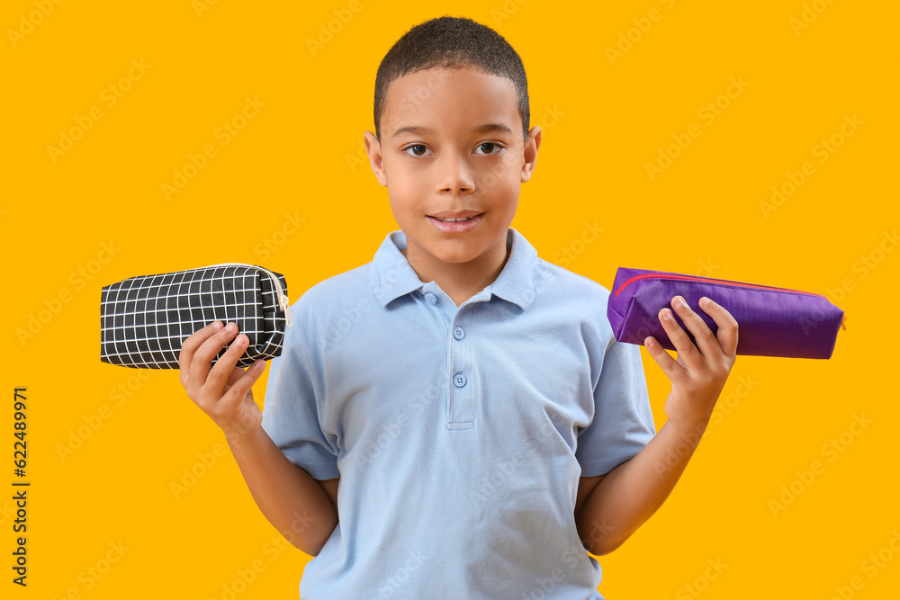 Little African-American boy with pencil cases on orange background