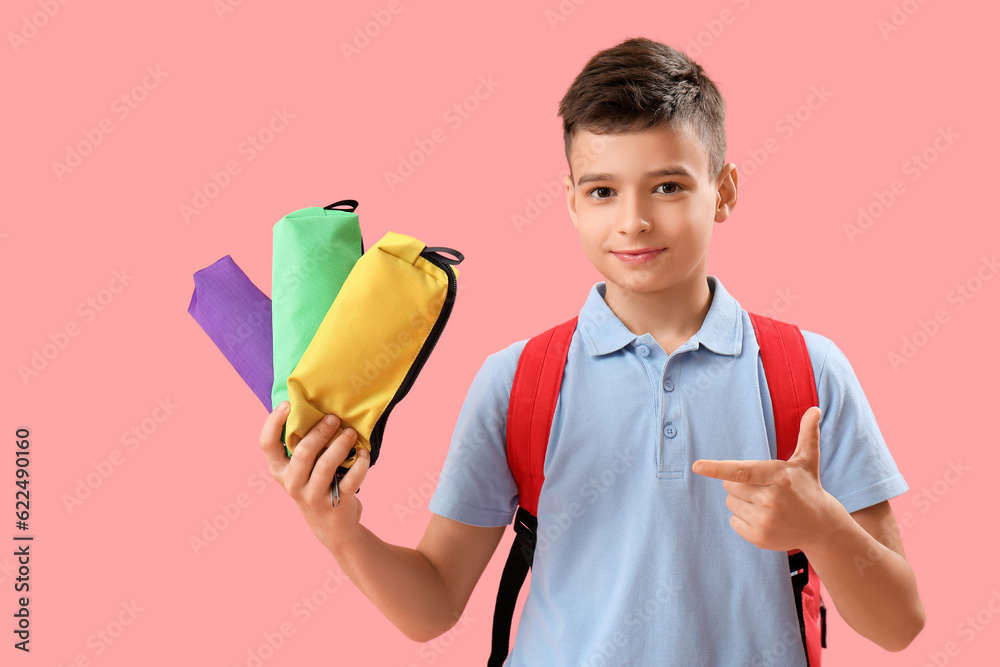 Little schoolboy pointing at pencil cases on pink background