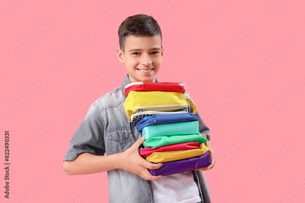 Little boy with pencil cases on pink background