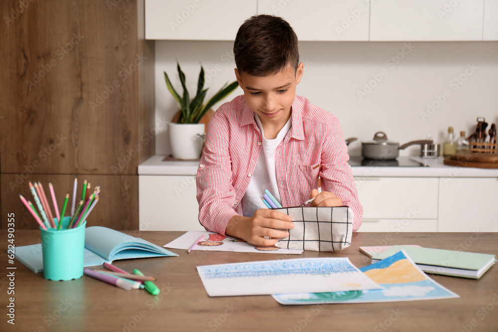 Little boy with pencil case at table in kitchen