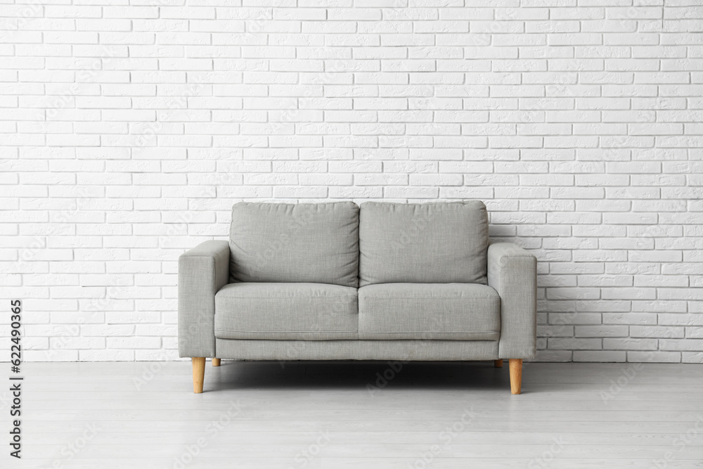 Cozy grey sofa near white brick wall