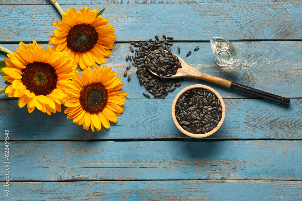 Sunflowers and bowl with seeds on blue wooden background