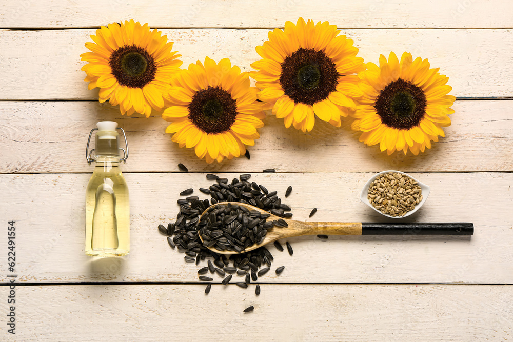 Sunflowers, spoon with seeds and bottle of oil on light wooden background