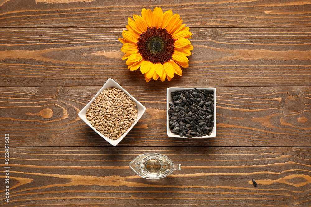 Sunflower, bowls with seeds and oil on wooden background