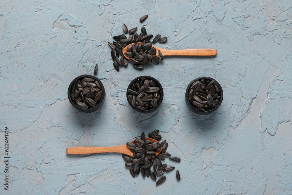 Bowls and spoons with sunflower seeds on blue background