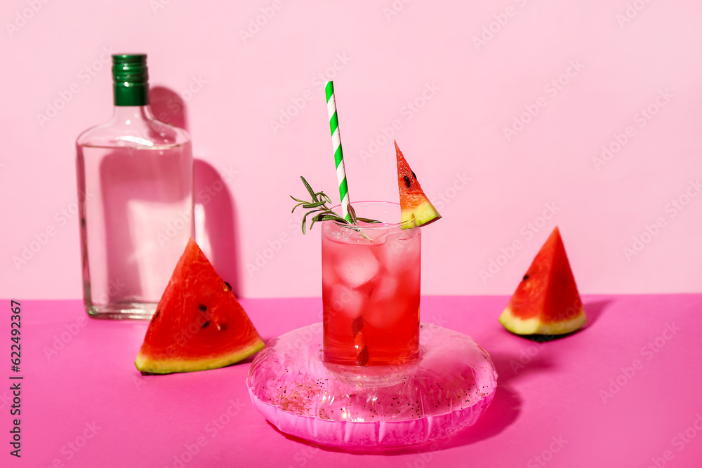 Glass of tasty watermelon cocktail with mini inflatable ring on pink table near wall