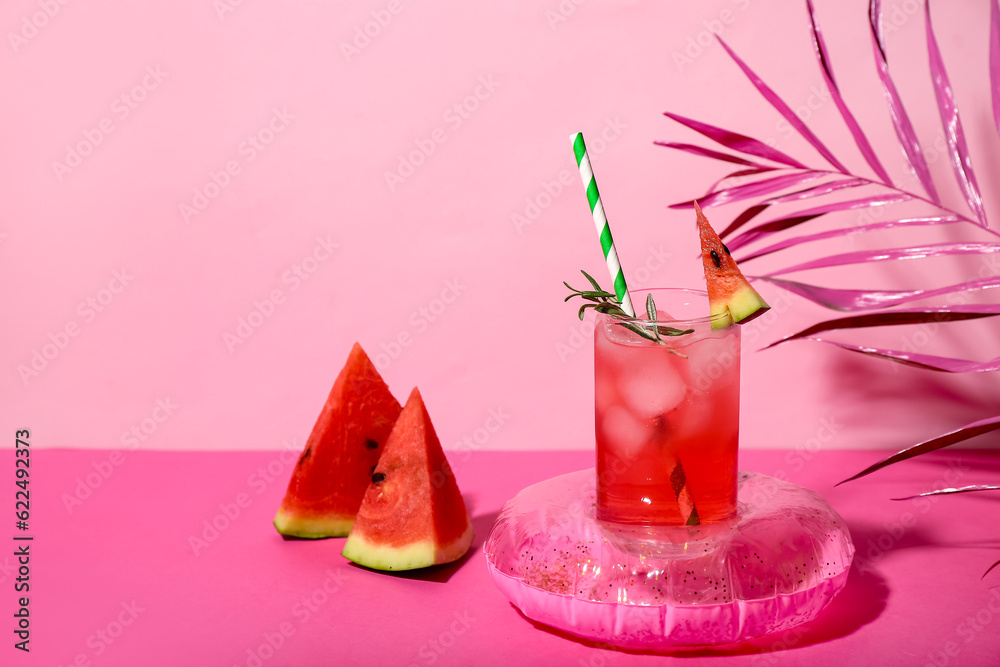 Glass of tasty watermelon cocktail with mini inflatable ring on pink table near wall