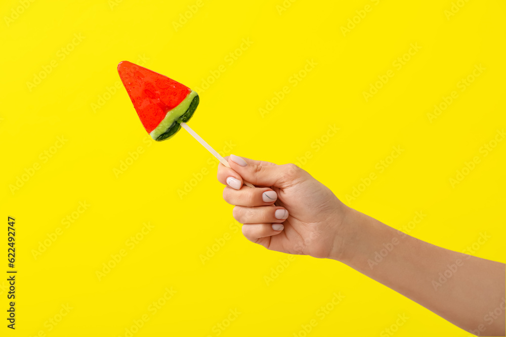 Woman holding lollipop in shape of watermelon slice on yellow background