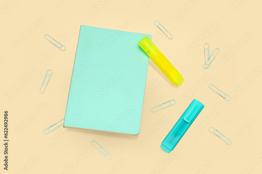 Notebook with different stationery on pale yellow background