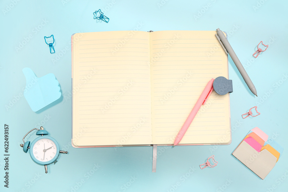 Blank notebook with stationery and alarm clock on blue background