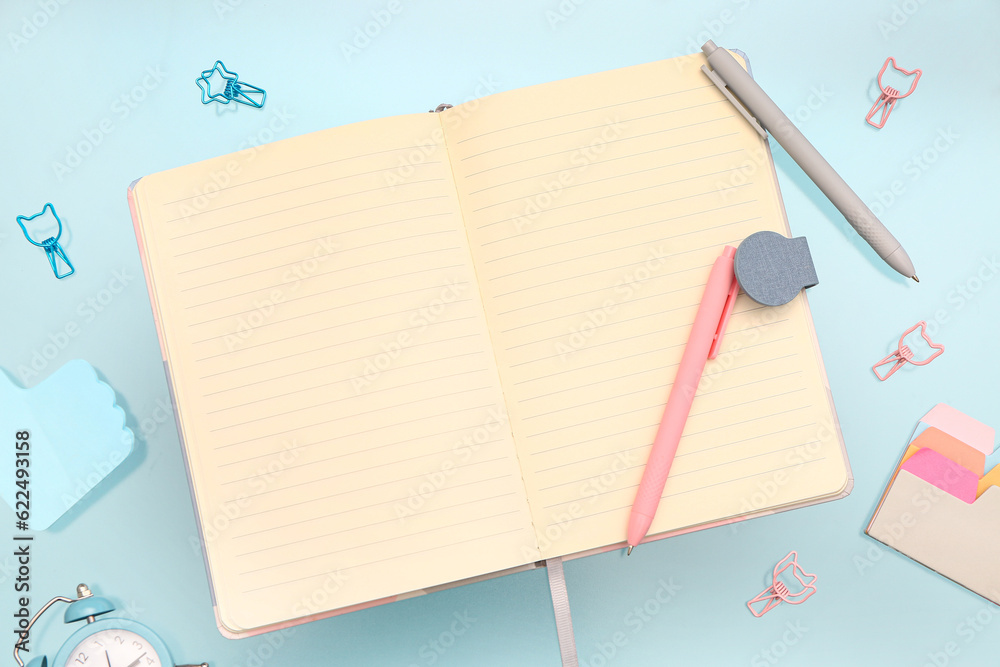 Blank notebook with stationery and alarm clock on blue background