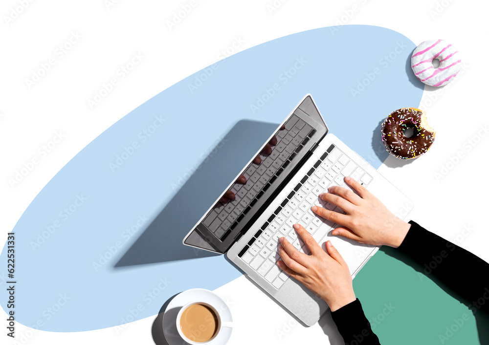 Person using a laptop computer with a donut and a cup of coffee - Flat lay