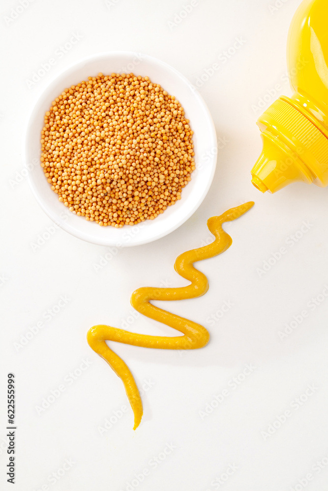 mustard seeds in a plate and squeezed yellow mustard sauce on white background. top view.