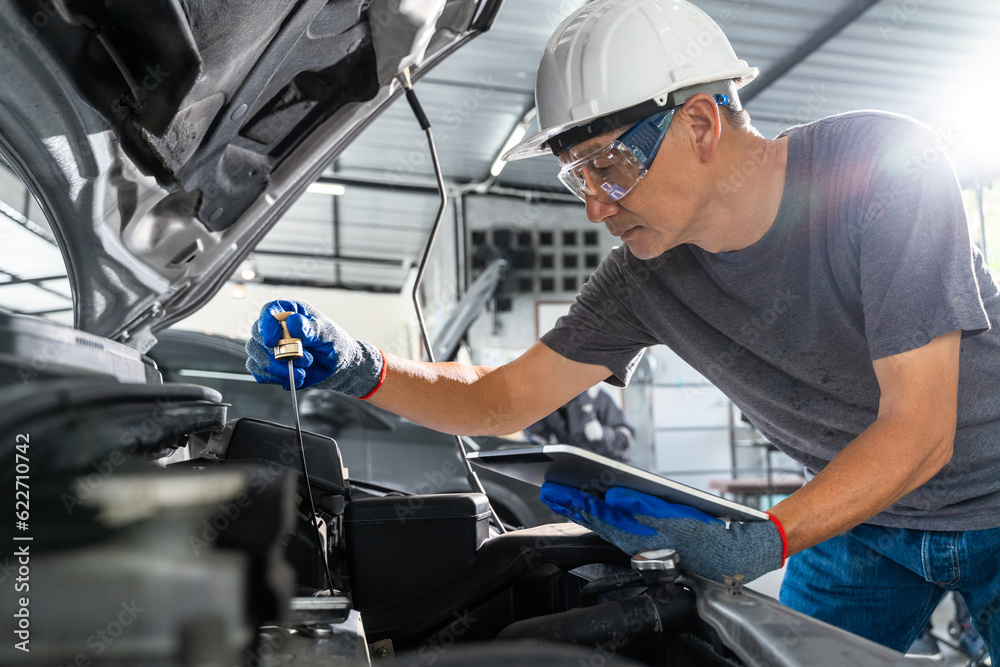 An Asian male car mechanic checking cars engine oil and working on repairing the car at car repair 