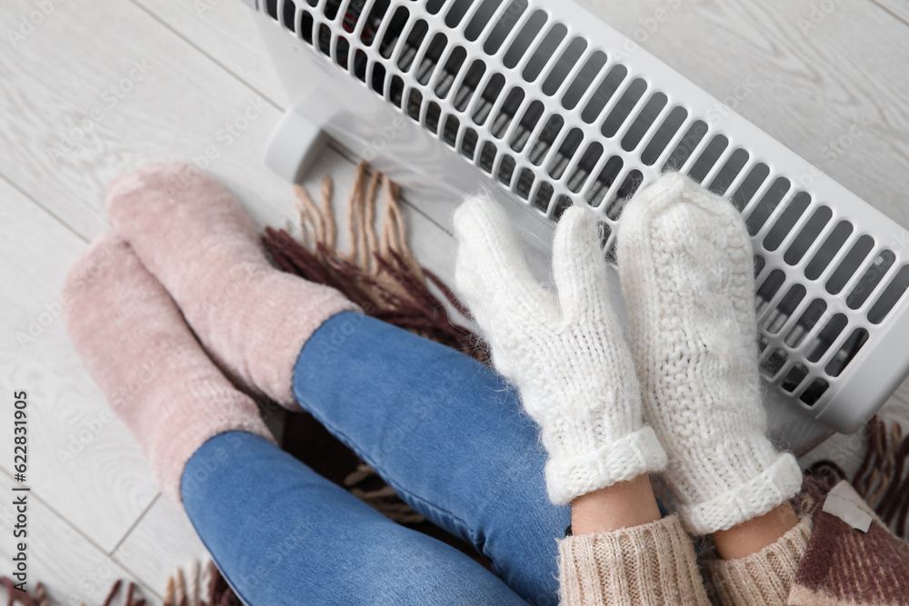 Woman warming hands in mittens near radiator at home, closeup