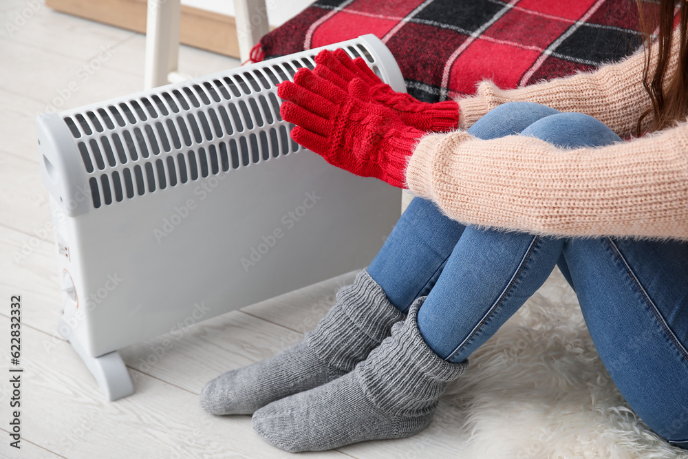 Woman warming hands in gloves near radiator at home, closeup