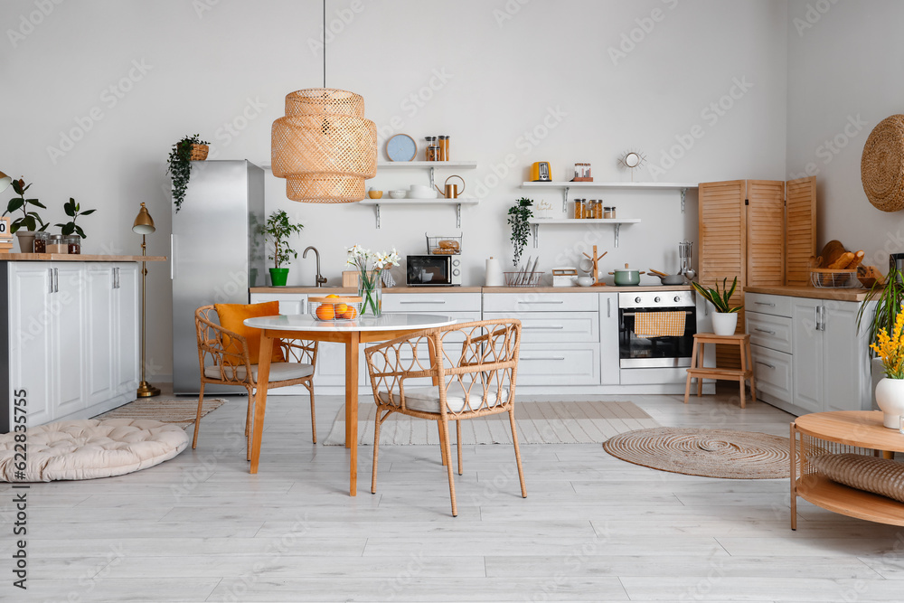 Interior of light kitchen with stylish fridge, counters, table and chairs