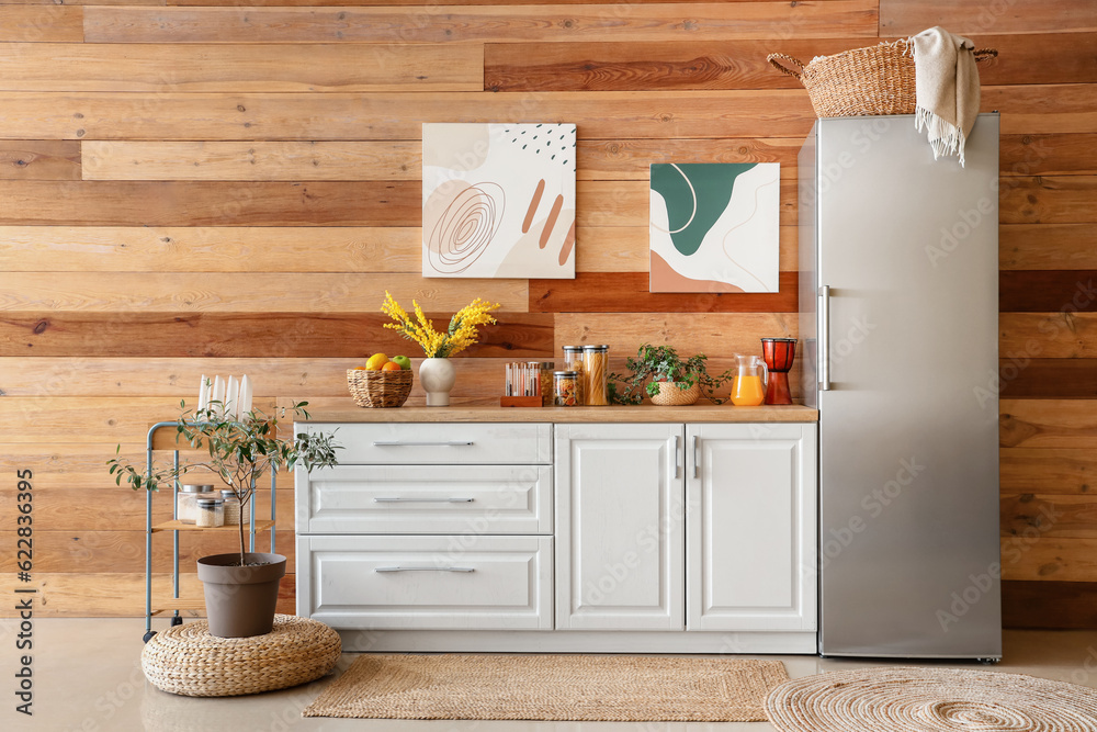 Interior of kitchen with stylish fridge, counters, pictures and houseplants