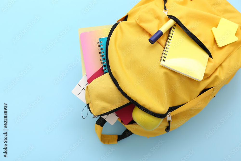 Yellow school backpack with pencil case, notebooks and apple on blue background