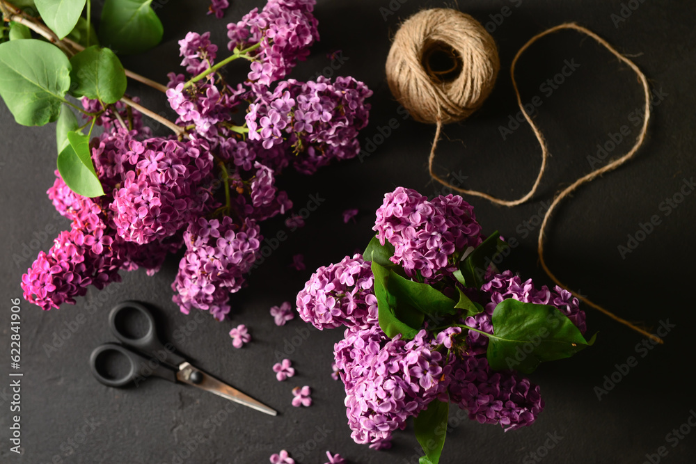 Beautiful lilac flowers with scissors and threads on dark background