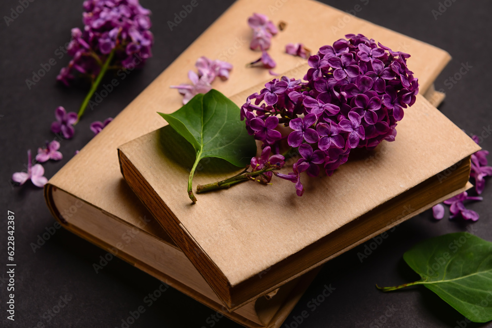 Beautiful lilac flowers and books on dark background, closeup