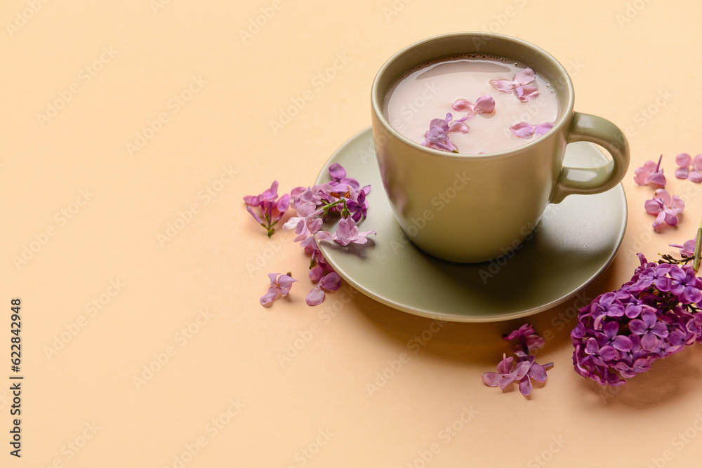 Cup of coffee and beautiful lilac flowers on beige background, closeup