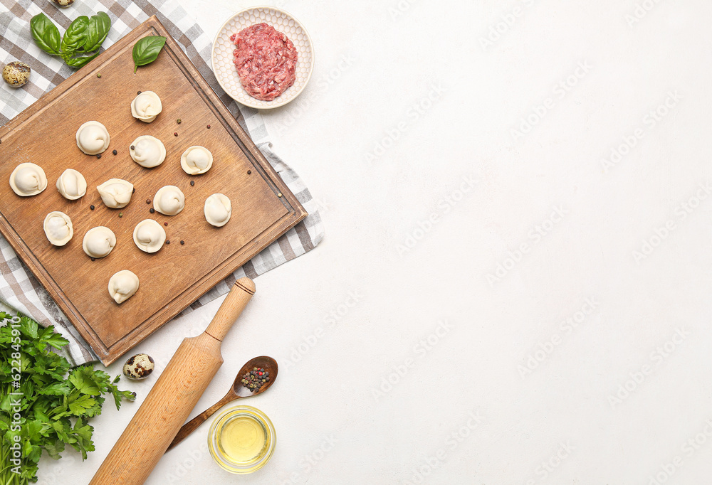 Board with uncooked dumplings and ingredients on light background