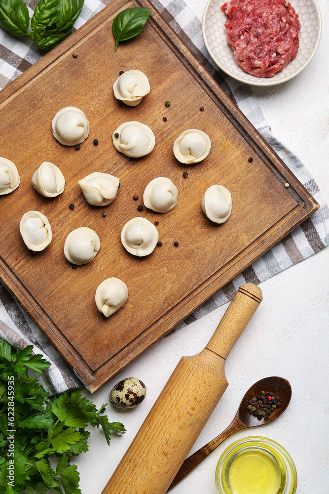 Board with uncooked dumplings and ingredients on light background