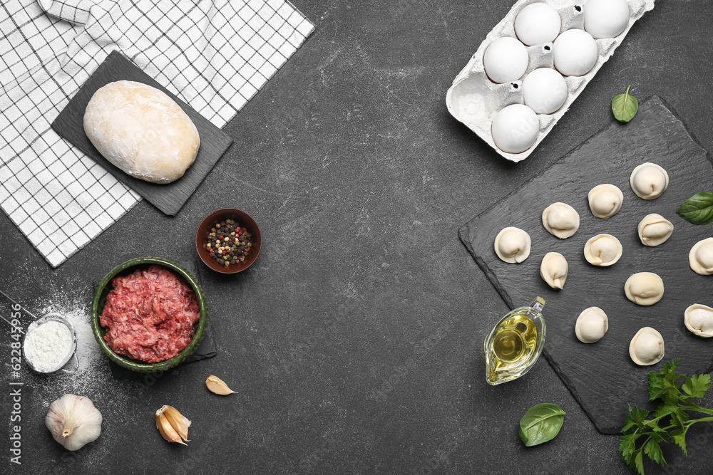 Board with uncooked dumplings and ingredients on black background