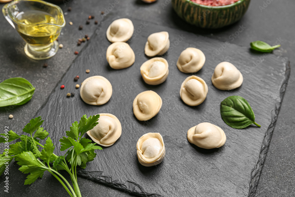 Board with uncooked dumplings on black background