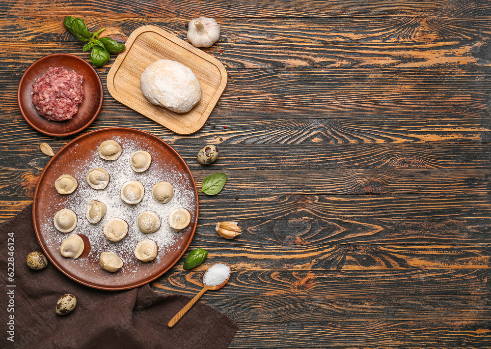 Plate with uncooked dumplings and ingredients on wooden background